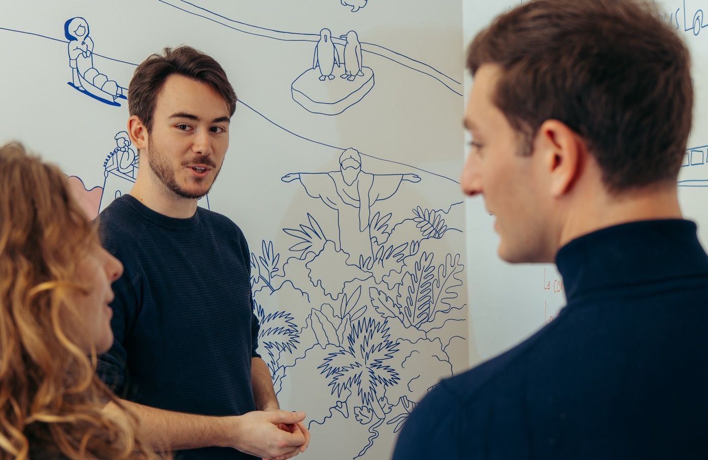 Trois personnes en conversation devant la fresque murale de l'école